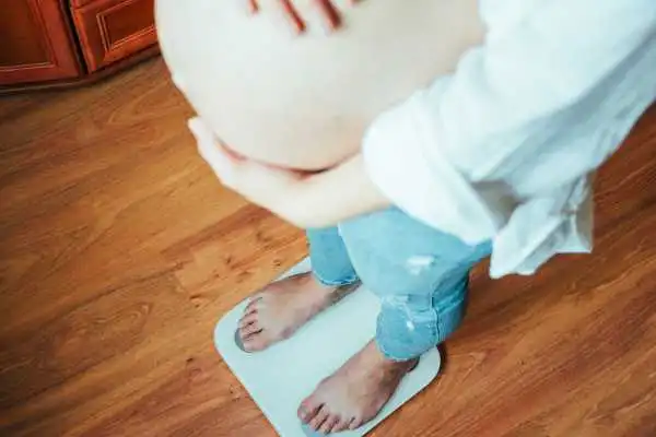 Image of woman weighing herself and experiencing weight gain through pregnancy Sheffield